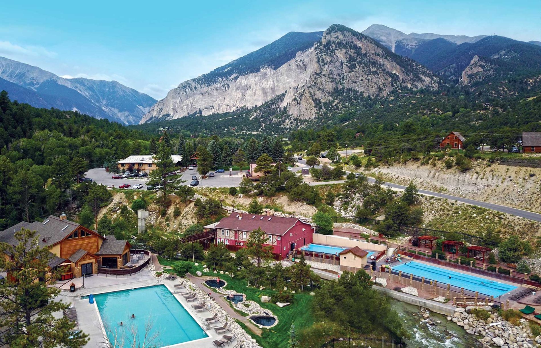 Aerial view of a mountain hot springs resort near Denver with outdoor pools and lodging amidst forested terrain